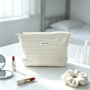 Detailed view of the cream knitted makeup pouch with herringbone texture on a white table.