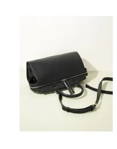 Detalle del bolso de mano tipo bowling en cuero negro con cierre de cremallera y correa ajustable.