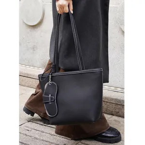 Vista detallada del bolso tote de cuero negro con costuras blancas y accesorio.