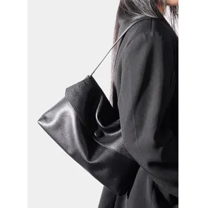 Detail view of a black genuine leather shoulder bag featuring textured finish and button flap closure.