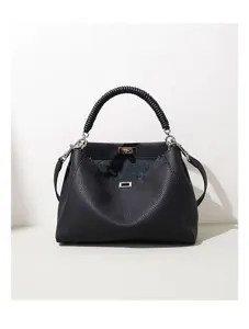 Detalle de primer plano del bolso de cuero negro con su asa única y mecanismo de bloqueo.