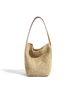 Close-up detail of the woven straw mesh texture and brown leather handle of the bucket bag.