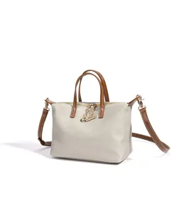 Vista dettagliata della borsa in tela beige con manici in pelle marrone e dettagli metallici dorati.