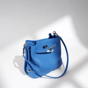 Blue leather bucket bag with top strap and metal lock closure, stylish commuter handbag.
