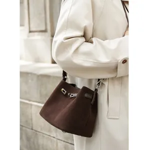 Detail shot of brown suede bucket bag with metallic turn-lock hardware and leather strap.