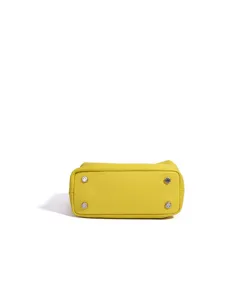 Vista detallada del fondo del bolso de cuero amarillo con cuatro tachuelas de metal plateado.