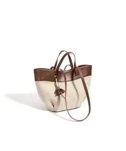 Canvas bucket bag detail showing linen texture and brown leather trim with pendant accessory.