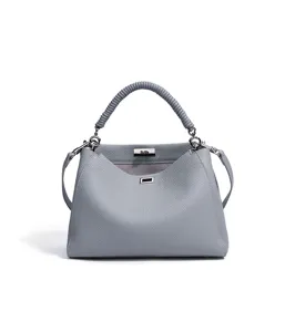 Primer plano detallado del bolso de cuero gris con asa envuelta y cierre metálico elegante.