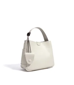 Minimalist off-white leather bucket bag with top handle and chic pendant detail for women.