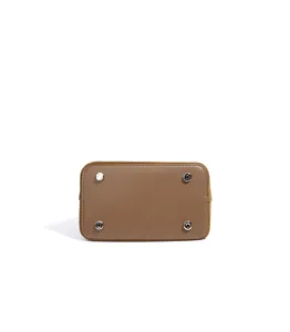 Bottom detail view of brown leather handbag featuring four protective metal feet and texture.