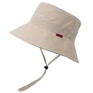 Détail de chapeau bob beige avec texte brodé, tissu imperméable et jugulaire réglable.
