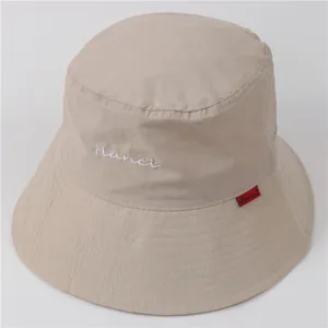 Vue détaillée d'un chapeau bob beige imperméable avec broderie et petite étiquette rouge.