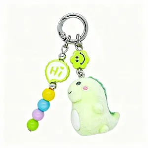 Close-up detail of cute flocked green dinosaur keychain with colorful beads and bag charm accessory.