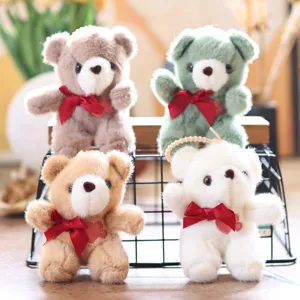 Close-up of cute teddy bear plush pendants with red bows, soft toy keychains on display.