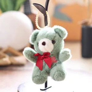 Close-up of fluffy green teddy bear plush pendant with red bow detail and pearl hanging loop.