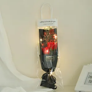 Transparent gift bag with artificial red roses, dried flowers, and LED fairy lights for gifts.