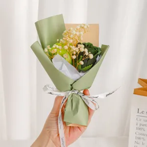 Mini preserved rose gypsophila bouquet detail shot, elegant green wrapping and ribbon.