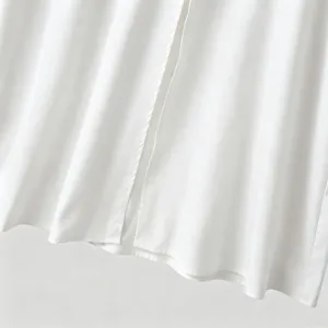 White garment fabric detail view, smooth texture and neat stitching hemline close-up shot.