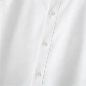 Close up detail of white textured men shirt fabric featuring matching buttons and clean stitching.
