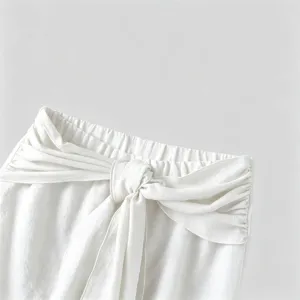 Close-up of white casual trousers waistband with stylish knot tie and pleated drape detail.