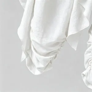 Detailed view of white casual trousers fabric with delicate ruching and layered drape design.
