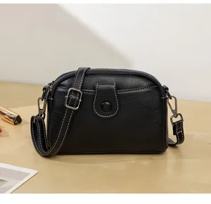 Black leather crossbody bag detail showing texture, white stitching and shoulder strap.
