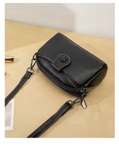 Close-up detail view of black leather crossbody bag featuring double zipper compartments.