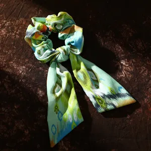 Close-up detail of green ethnic style printed fabric hair scrunchie with ribbon bow.