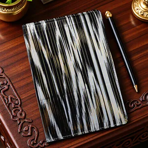 Detailed view of the Xinjiang ethnic style fabric notebook with black and gold pattern and pen.
