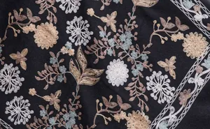 Detailed close-up of ethnic floral embroidery on a soft black imitation cashmere shawl fabric.
