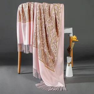 Close-up view of a pink cashmere-feel shawl with golden paisley embroidery and stylish fringe.