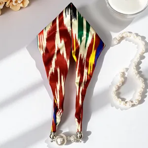 Vista dettagliata di foulard in seta con stampa ikat e chiusura magnetica con perla pendente.