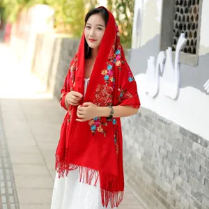 Detailed view of a red embroidered cashmere scarf with colorful floral patterns and tassels.