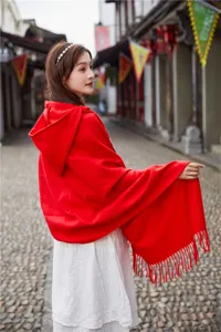 Red hooded cape shawl detail, ethnic style tassel poncho, outdoor scenic street view fashion.