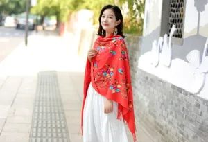 Detailed view of a vibrant red cashmere shawl featuring intricate floral embroidery and tassels.