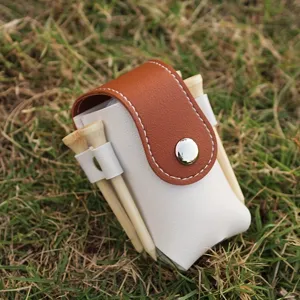 Closeup of portable white and brown leather golf tee pouch with wooden tees on grass.
