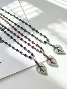 Detailed shot of sparkling leaf pendant necklaces featuring vibrant colorful zirconia and chains.
