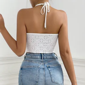 Backless white halter crop top featuring chic eyelet embroidery paired with classic jeans.
