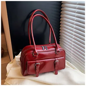Detail view of red glossy leather underarm pillow bag with double handles and front buckles.