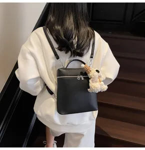 Detail view of the black pebbled leather women backpack featuring a cute plush puppy charm.