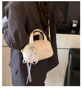 Detail shot of women's trendy soft leather shoulder bag with elegant pearl lace bow charm.