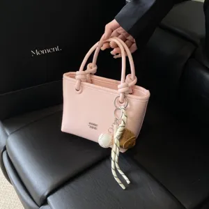 Primo piano di una borsa rosa chic con manici annodati e un simpatico ciondolo da baseball.
