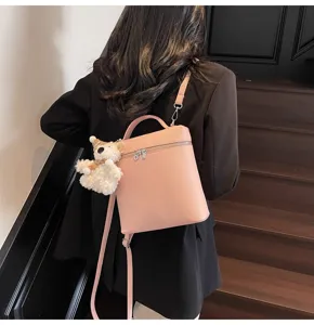Detail view of the pink litchi pattern leather backpack showing the cute plush bear pendant.