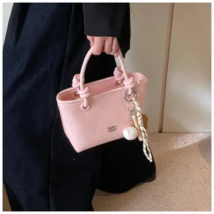 Elegante borsa a mano rosa in vera pelle con manici annodati e ciondolo da baseball dettaglio.