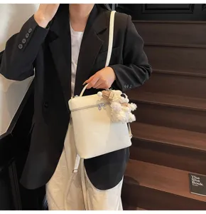 Detail view of white leather texture bucket bag with cute bear charm, elegant styling.