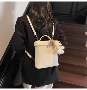 Detailed view of a stylish white litchi grain small backpack with cute plush pendant.