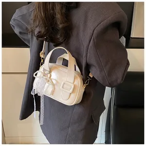 White patent leather handbag detail view, showing elegant lace pearl bow and shoulder strap.
