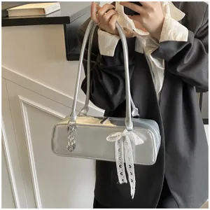Silver metallic baguette shoulder bag detail featuring lace bow and metal heart charm decor.