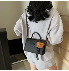Detail view of a chic black textured crossbody small square bag with a cute fuzzy bear pendant.