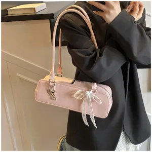 Pink patent leather baguette shoulder bag detail showing bow and heart charm, stylish accessory.